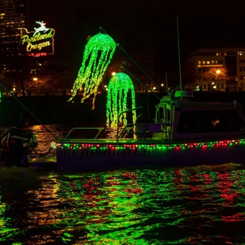 A boat decorated with bright green and red lights, including glowing jellyfish shapes, cruises on water at night.