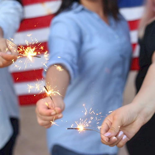 People holding sparklers in front of an American flag, sparks flying as they celebrate together.
