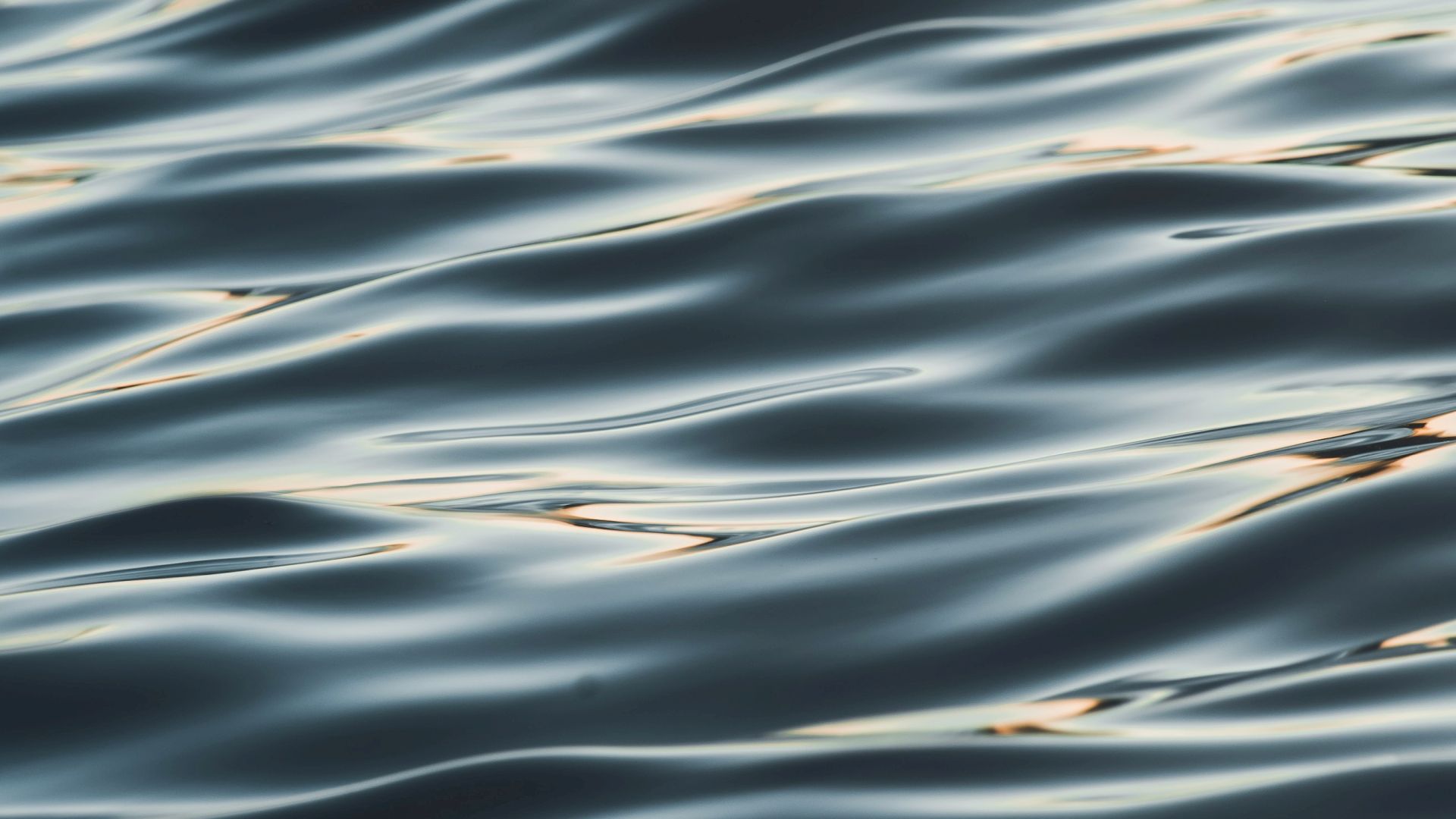 Close-up of ocean water with shimmering ripples and streaks of light, blurred for a smooth, flowing feel.