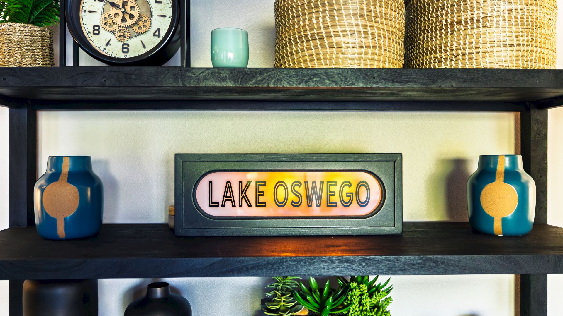 A mantel shelf with a big clock, two woven baskets, blue vases, and a &ldquo;LAKE OSWEGO&rdquo; sign.