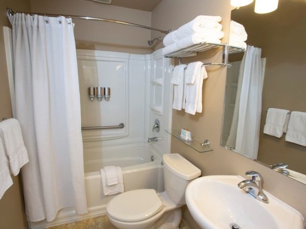 A clean bathroom with white towels, a shower, sink, toilet, and mirror. The space is organized and well-lit, creating a neat appearance.