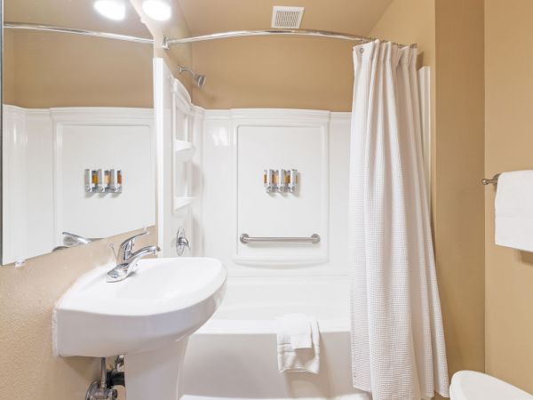 A compact bathroom with a white sink, a shower/tub combo with a curtain, a wall mirror, and a towel rack.