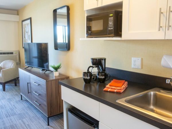 A hotel room kitchenette with a sink, microwave, coffee maker, TV, and seating area.