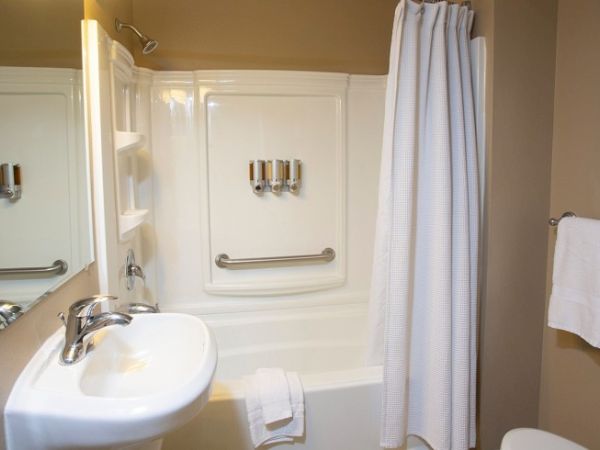 The image shows a bathroom with a sink, a bathtub with a curtain, a towel rack, and wall-mounted amenities.