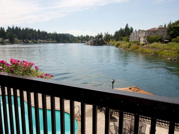A scenic view of a lake with surrounding trees, houses, and a pool. The image is taken from a balcony with a black railing.