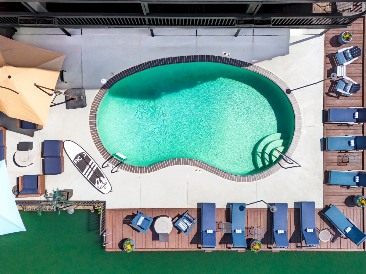 A top-down view of a backyard resort with a turquoise swimming pool, lounge chairs, and wooden decks surrounding it.