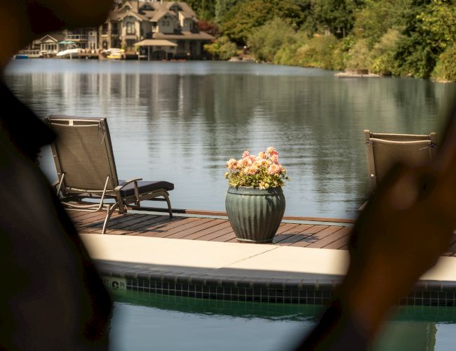 The image shows a silhouette of a person by a lake or pool, with lounge chairs and a potted plant on a dock, surrounded by trees.
