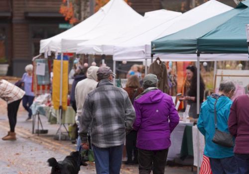 People are shopping at an outdoor market with tents and stalls, set on an autumn day.
