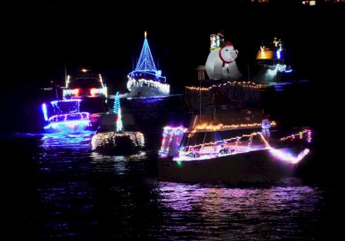 The image shows boats decorated with colorful lights and festive ornaments floating on water at night.