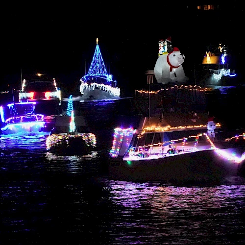 The image shows boats decorated with colorful lights and festive ornaments floating on water at night.
