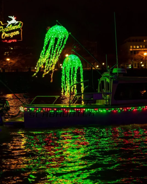A boat decorated with bright green and red lights, including glowing jellyfish shapes, cruises on water at night.