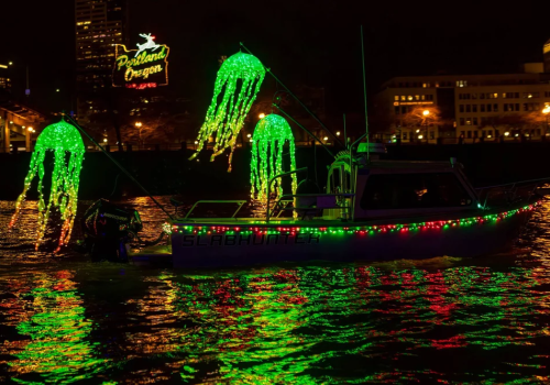 A boat decorated with bright green and red lights, including glowing jellyfish shapes, cruises on water at night.