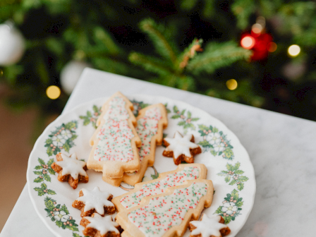 A plate of Christmas-themed cookies shaped like trees and stars, decorated with white icing and colorful sprinkles, on a festive plate.