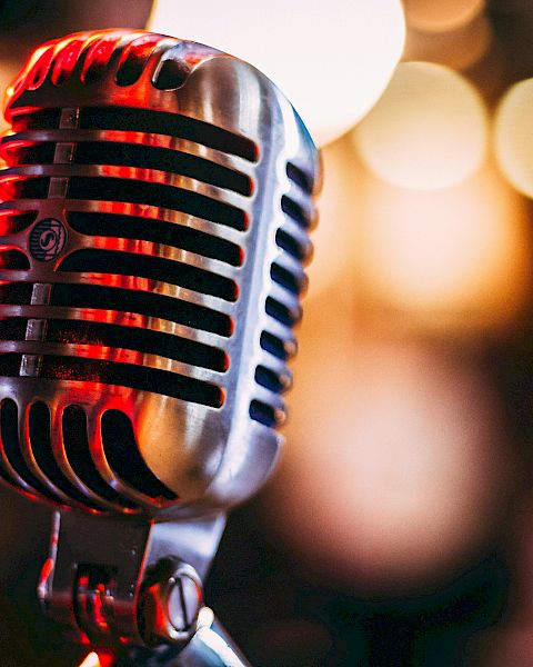 A vintage microphone on a stand in a dim, bokeh-lit stage setting.
