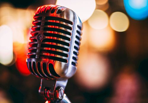 A vintage microphone on a stand in a dim, bokeh-lit stage setting.