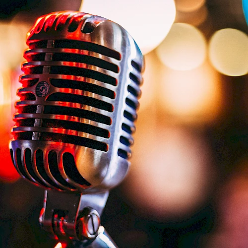 A vintage microphone on a stand in a dim, bokeh-lit stage setting.