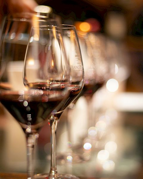 Wine glasses on a bar, close-up with warm ambient lights in the background, blurred bottles and reflections.