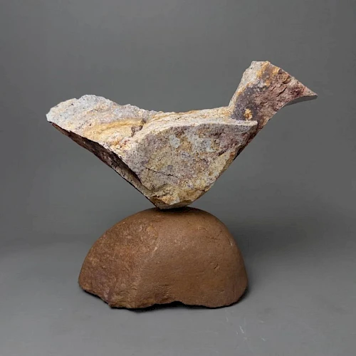 A sculpture of a stylized bird perched on a rounded pedestal, made from rough, layered clay or stone with a weathered finish.