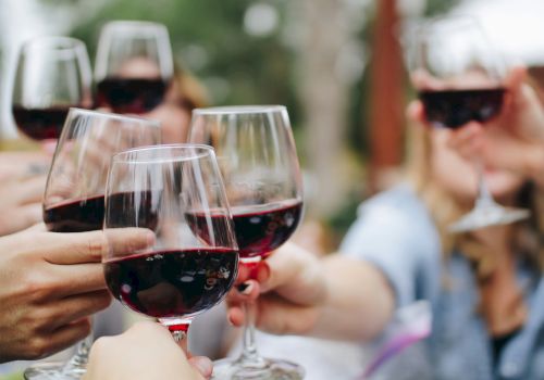 People clinking wine glasses in a toasting cheers, enjoying red wine together.