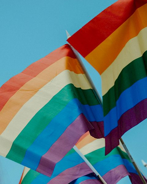 Several rainbow Pride flags waving in the wind against a blue sky, symbolizing LGBTQ+ pride and inclusivity, vibrant colors fluttering brightly.