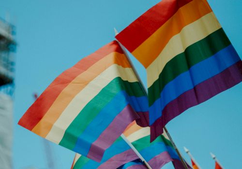 Several rainbow Pride flags waving in the wind against a blue sky, symbolizing LGBTQ+ pride and inclusivity, vibrant colors fluttering brightly.