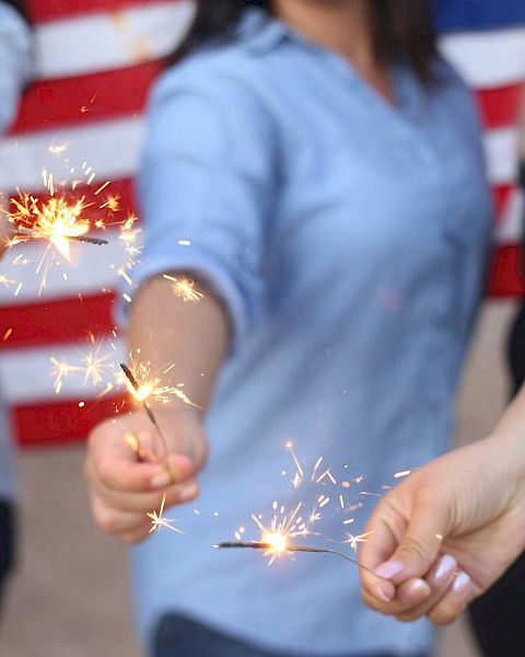 People holding sparklers in front of an American flag, sparks flying as they celebrate together.