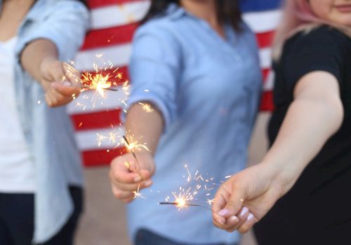 People holding sparklers in front of an American flag, sparks flying as they celebrate together.